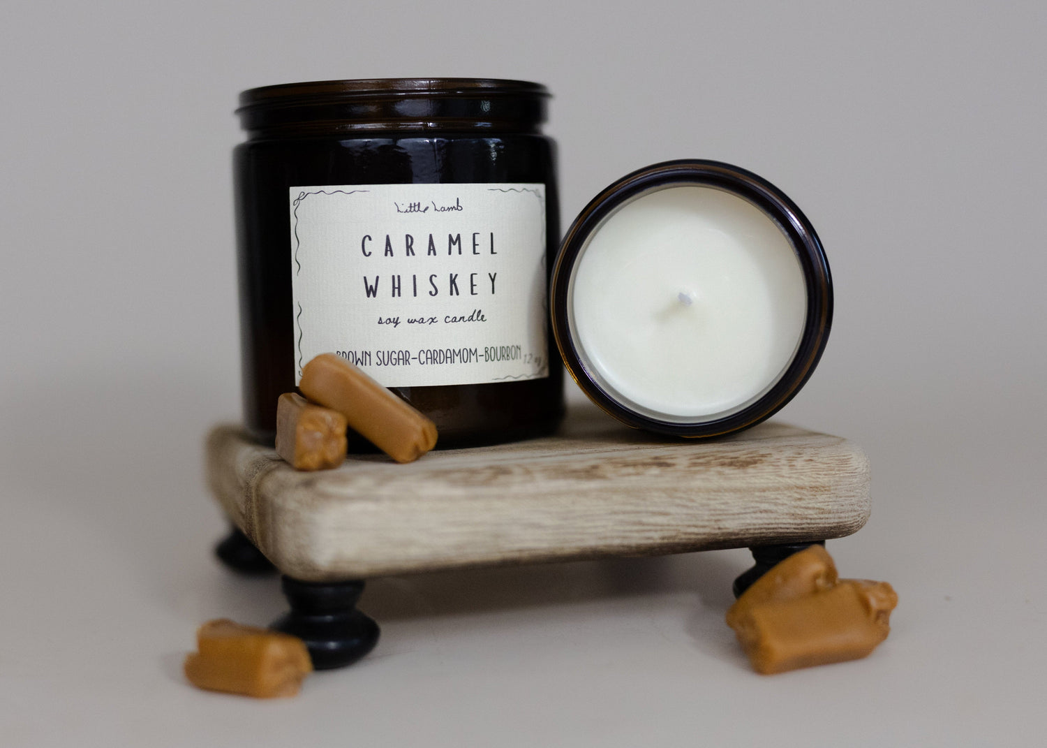 Candle and jar labeled 'Caramel Whiskey' on a wooden stand with small wooden blocks.