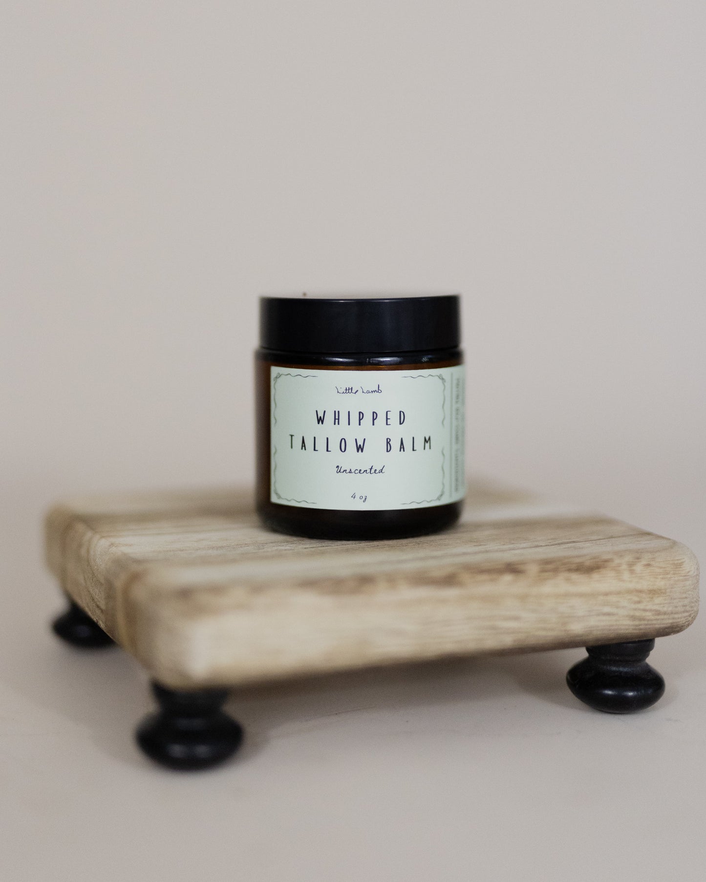 Jar of whipped tallow balm on a wooden stand with a neutral background