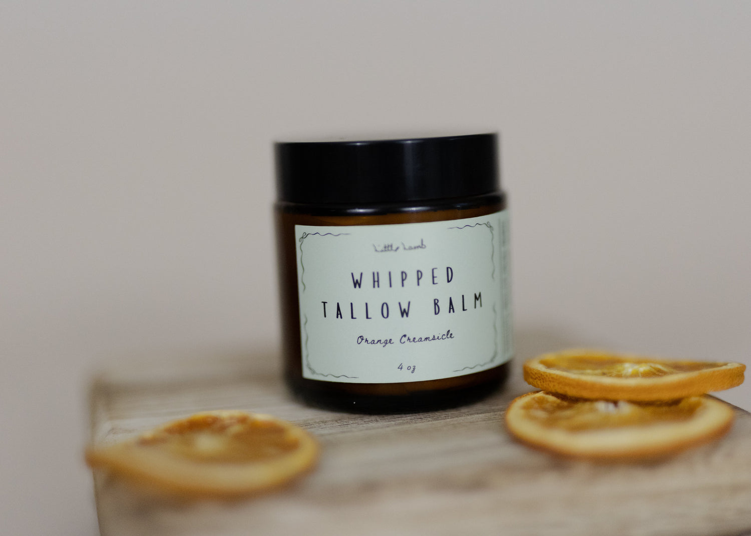 Jar of 'Whipped Tallow Balm' with dried orange slices on a wooden board