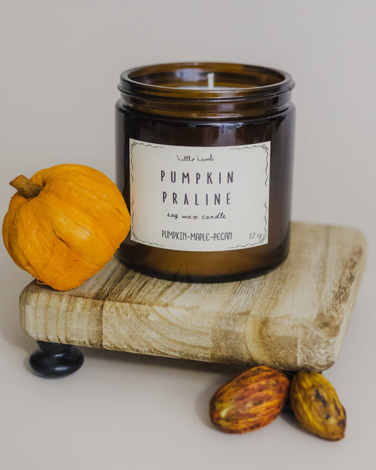 Candle labeled 'Pumpkin Praline' on a wooden block with pumpkins and gourds.