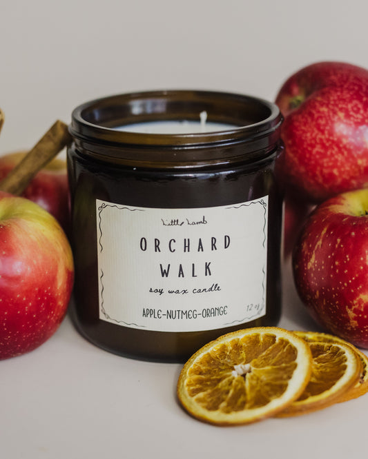 Candle labeled 'Orchard Walk' surrounded by apples and orange slices on a neutral background