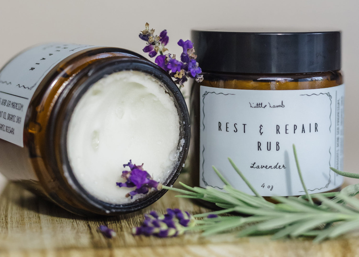 Two jars of 'Best & Repair Rub' with lavender flowers on a wooden surface.