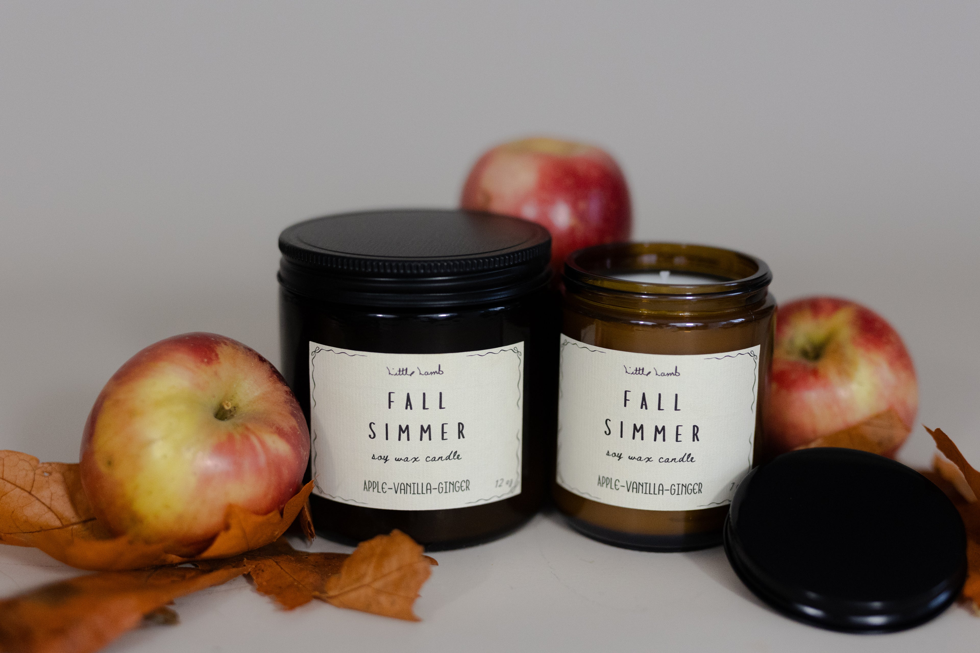 Two 'Fall Simmer' candles with apples and leaves on a neutral background