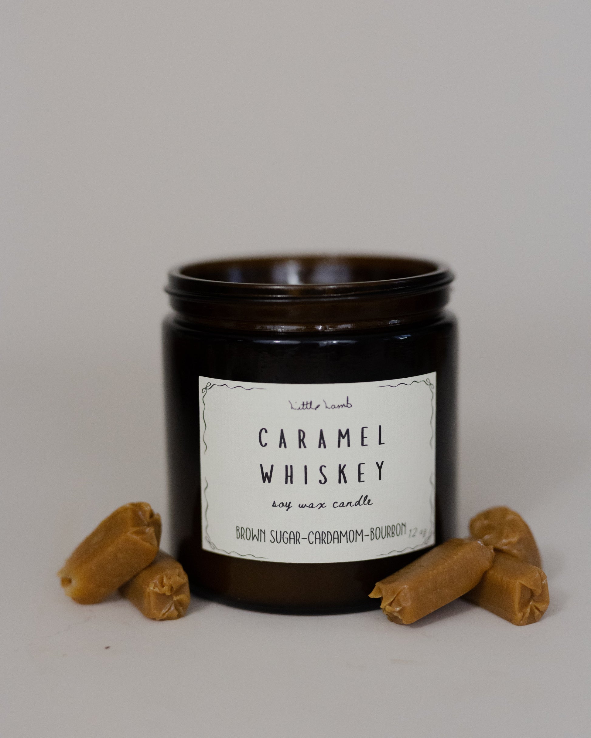 Candle jar labeled 'Caramel Whiskey' with two small brown objects on a gray background