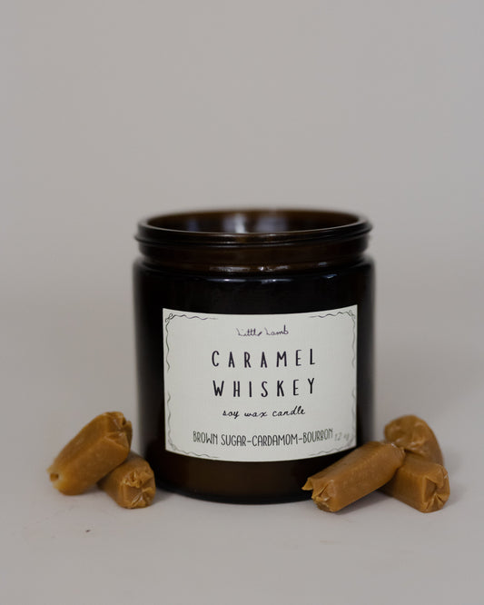 Candle jar labeled 'Caramel Whiskey' with two small brown objects on a gray background