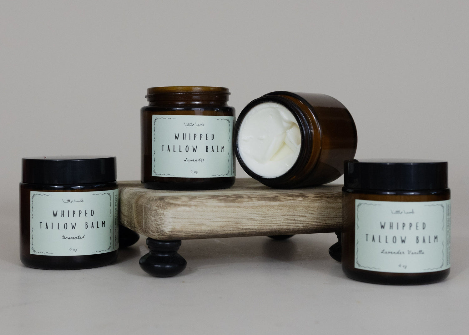 Four jars of 'Whipped Tallow Balm' on a wooden stand with a plain background