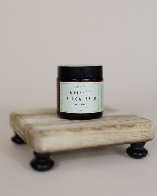 Jar of whipped tallow balm on a wooden stand with a neutral background
