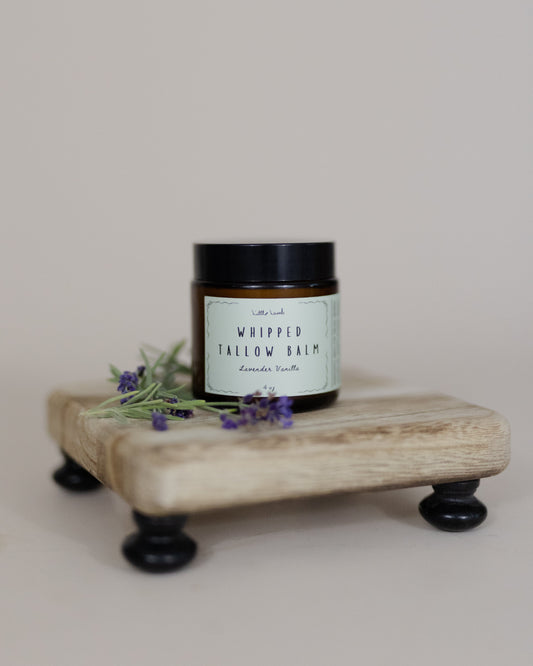 Jar of 'Whipped Yallow Balm' on a wooden stand with lavender flowers on a light background