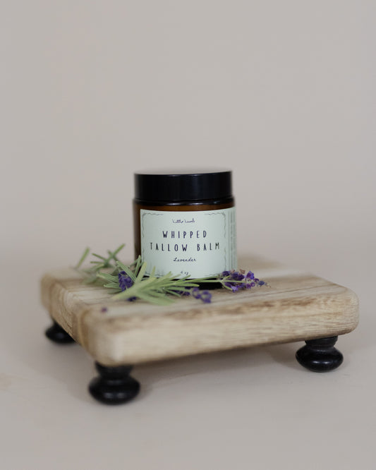 Jar of whipped tallow balm on a wooden stand with lavender flowers on a light background