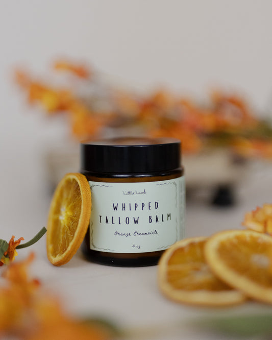 Jar of whipped tallow balm with dried oranges and flowers on a light background