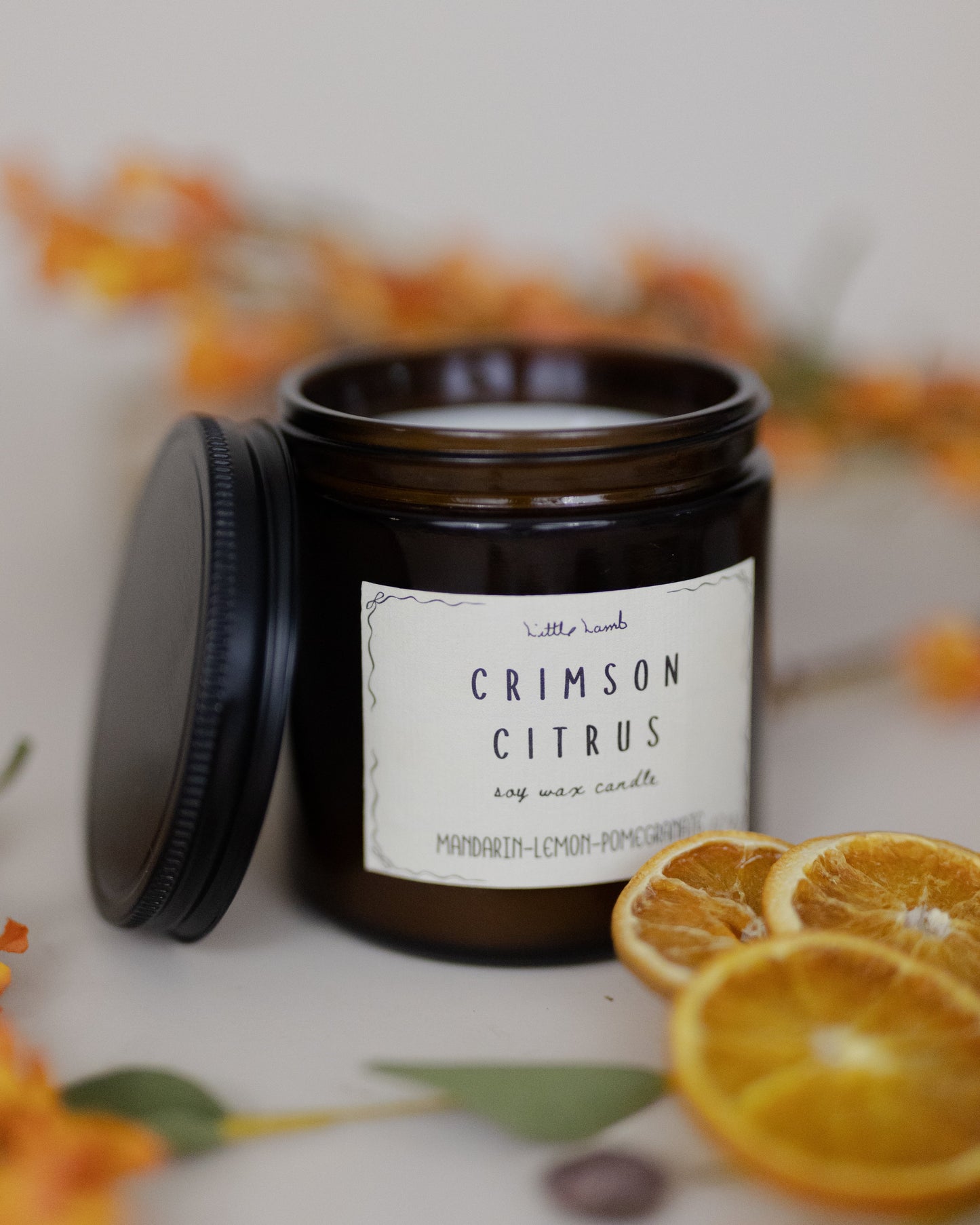 Candle jar labeled 'Crimson Citrus' with orange slices and flowers in the background