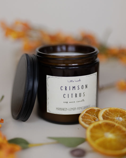 Candle jar labeled 'Crimson Citrus' with orange slices and flowers in the background